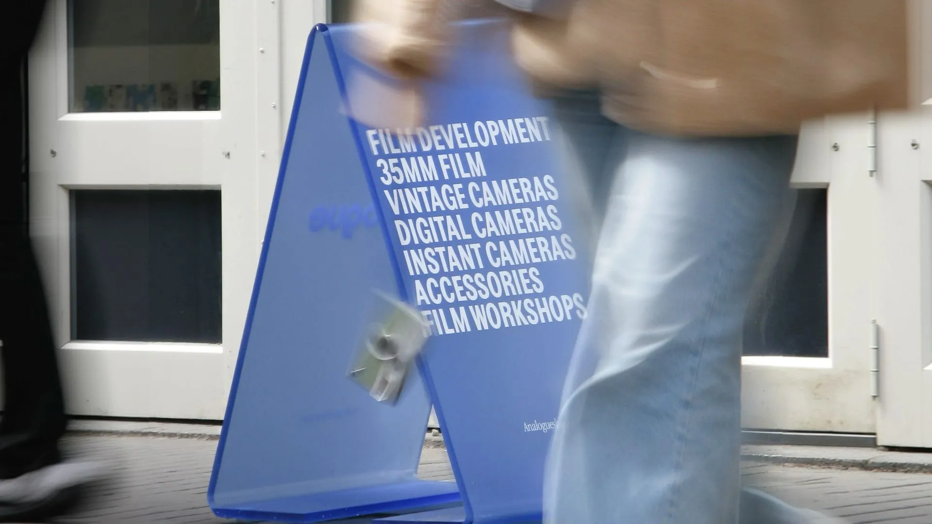 Blue sidewalk sign listing film development and cameras outside the shop, Analogue store Zeedijk